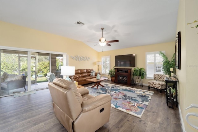 living room featuring visible vents, a ceiling fan, a glass covered fireplace, vaulted ceiling, and wood finished floors