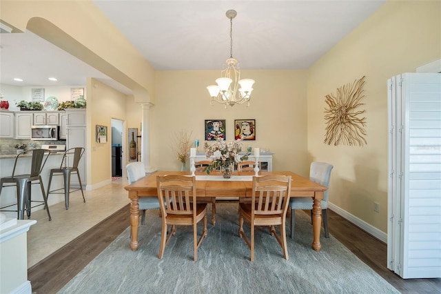 dining area featuring light wood-type flooring, ornate columns, baseboards, and a chandelier