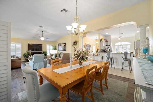 dining area with arched walkways, decorative columns, lofted ceiling, visible vents, and ceiling fan with notable chandelier