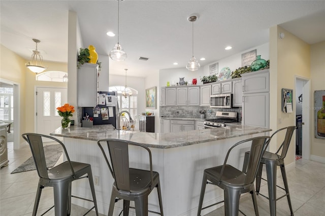 kitchen with light stone counters, a peninsula, a breakfast bar, appliances with stainless steel finishes, and backsplash