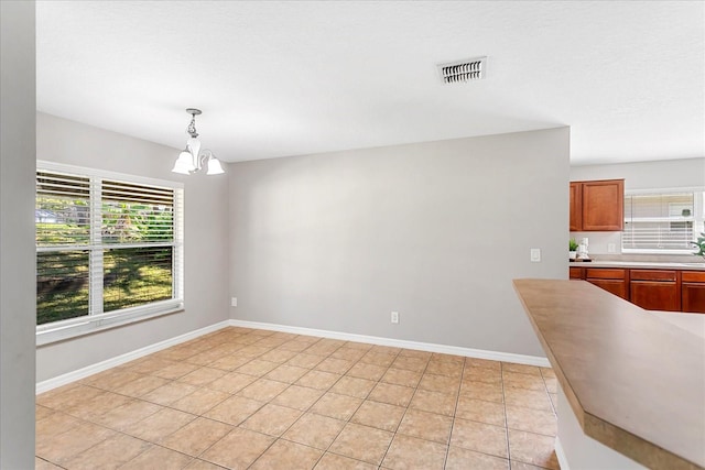 unfurnished dining area featuring a healthy amount of sunlight, baseboards, visible vents, and a chandelier