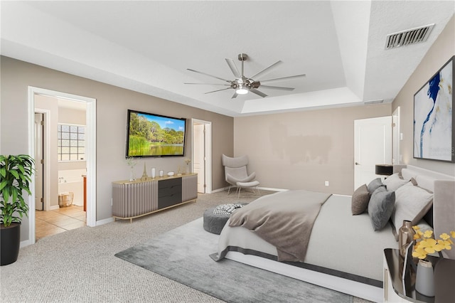 carpeted bedroom featuring a raised ceiling, visible vents, baseboards, and ensuite bath