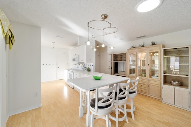 kitchen with light wood-style flooring, white appliances, light countertops, and a peninsula