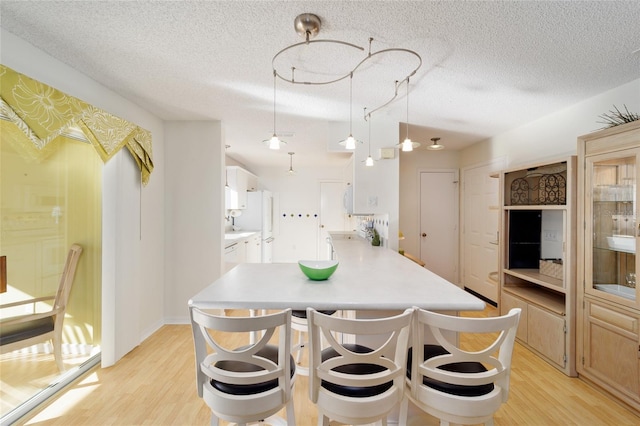 kitchen with light wood finished floors, a textured ceiling, a peninsula, a breakfast bar area, and light countertops