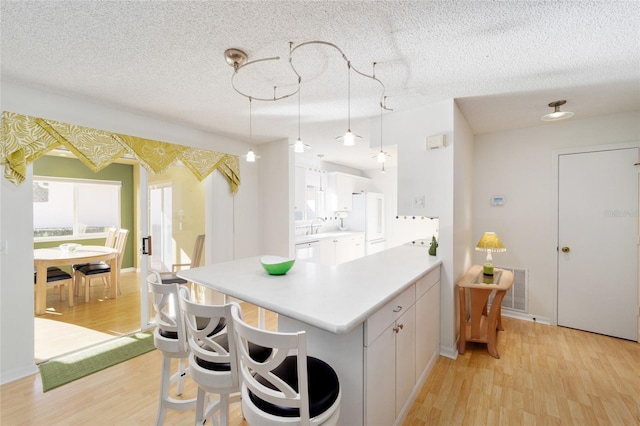 kitchen with light countertops, a peninsula, light wood-style floors, white dishwasher, and white cabinetry
