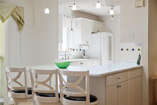kitchen with pendant lighting, a sink, freestanding refrigerator, a peninsula, and light countertops