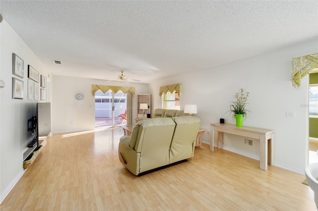 living room featuring visible vents, light wood-style flooring, and a textured ceiling