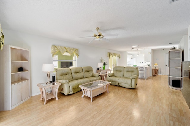 living area featuring light wood-style flooring, plenty of natural light, a ceiling fan, and a textured ceiling