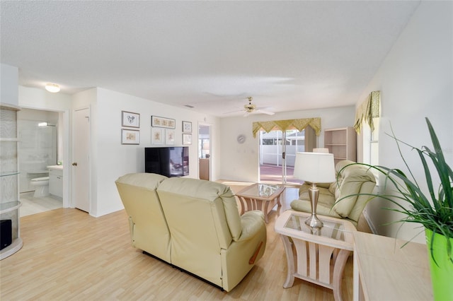 living area featuring a ceiling fan, light wood finished floors, and a textured ceiling