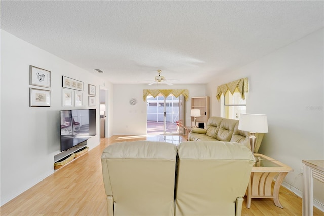living area featuring visible vents, a textured ceiling, light wood-type flooring, and ceiling fan