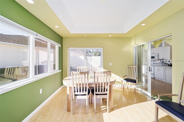 dining room with recessed lighting, baseboards, light wood-type flooring, and a tray ceiling