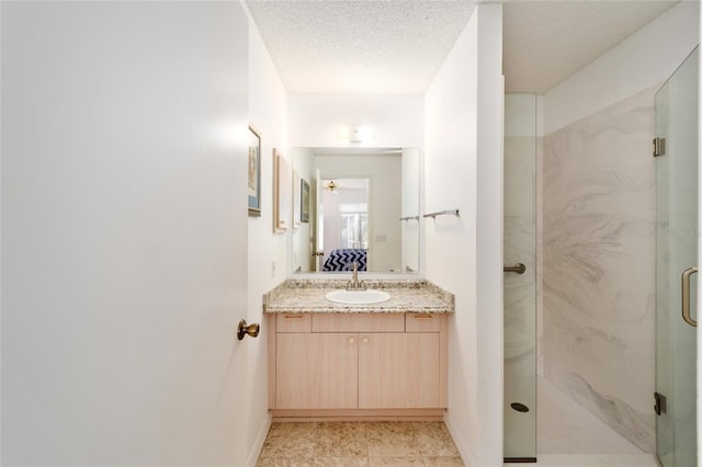 ensuite bathroom with a marble finish shower, connected bathroom, baseboards, vanity, and a textured ceiling