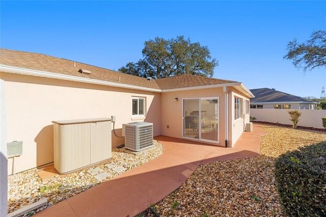 back of house with fence, roof with shingles, central AC unit, stucco siding, and a patio area