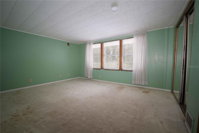 carpeted empty room with visible vents, crown molding, and baseboards