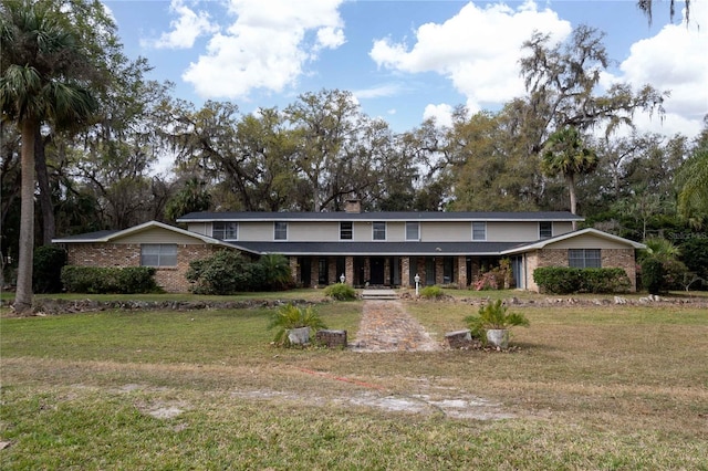 view of front of house featuring a front lawn, covered porch, brick siding, and a chimney