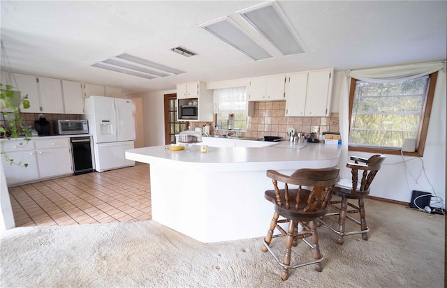 kitchen featuring visible vents, tasteful backsplash, white fridge with ice dispenser, and stainless steel microwave