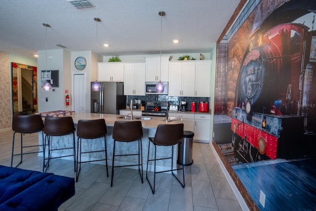 kitchen featuring a center island with sink, visible vents, a breakfast bar, stainless steel appliances, and backsplash
