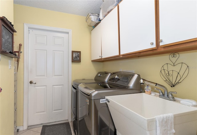 clothes washing area featuring cabinet space, light tile patterned floors, washing machine and clothes dryer, a textured ceiling, and a sink