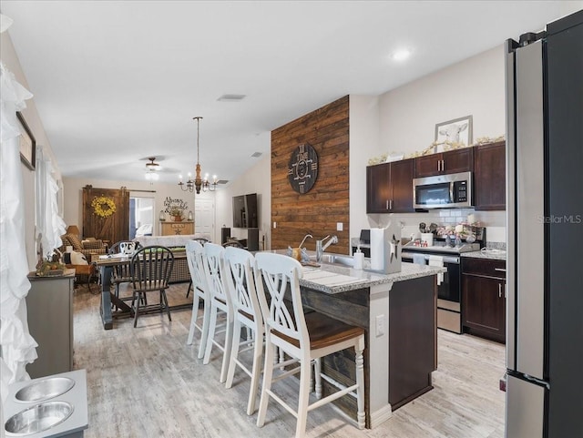 kitchen featuring stainless steel appliances, dark brown cabinetry, vaulted ceiling, and a sink