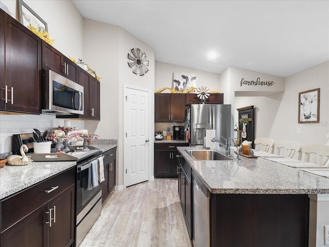 kitchen with a sink, light wood-style floors, dark brown cabinets, appliances with stainless steel finishes, and a center island with sink