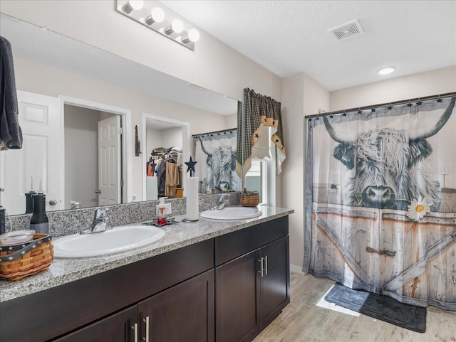 full bathroom featuring double vanity, wood finished floors, a sink, and visible vents