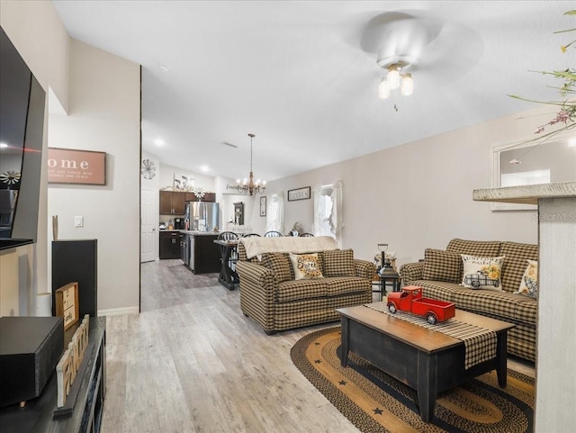 living area with vaulted ceiling, light wood-style flooring, and ceiling fan with notable chandelier