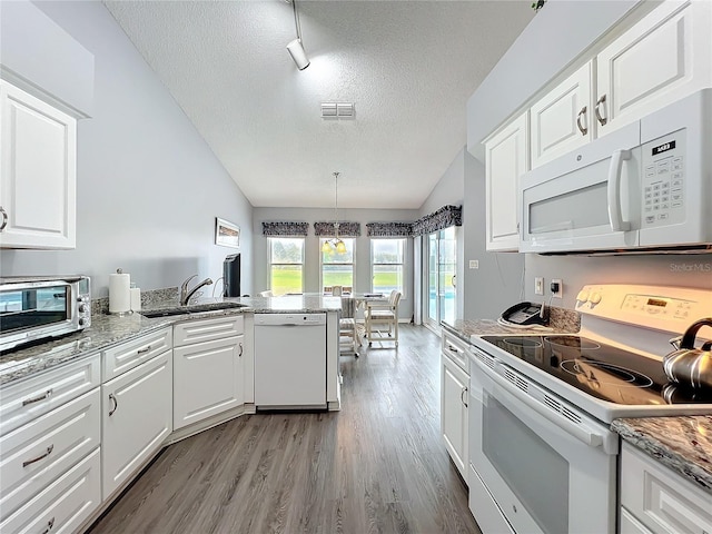 kitchen featuring white appliances, white cabinets, lofted ceiling, a peninsula, and a sink