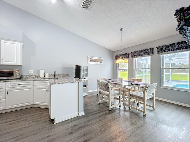 kitchen with a toaster, visible vents, a peninsula, vaulted ceiling, and white cabinetry