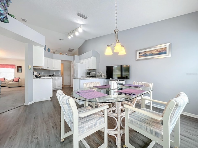 dining room with lofted ceiling, visible vents, an inviting chandelier, wood finished floors, and baseboards