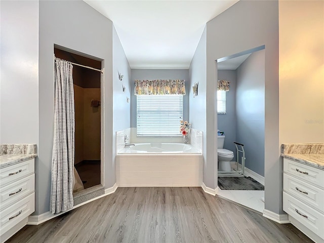 bathroom with toilet, wood finished floors, a garden tub, vanity, and a shower stall