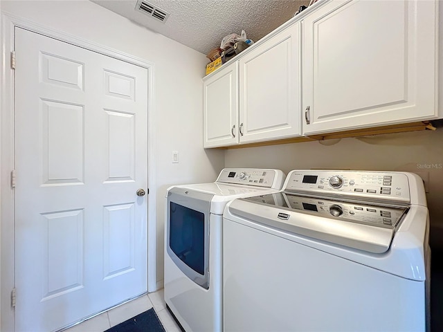 laundry area featuring cabinet space, visible vents, a textured ceiling, washing machine and dryer, and light tile patterned flooring