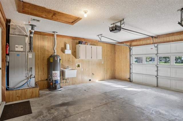 garage featuring wooden walls, visible vents, a garage door opener, water heater, and a sink