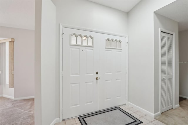 foyer entrance with baseboards, light colored carpet, and light tile patterned flooring