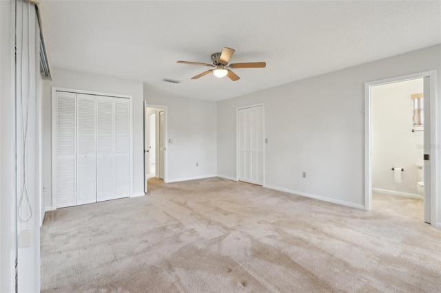 unfurnished bedroom featuring baseboards, visible vents, ensuite bath, carpet flooring, and two closets