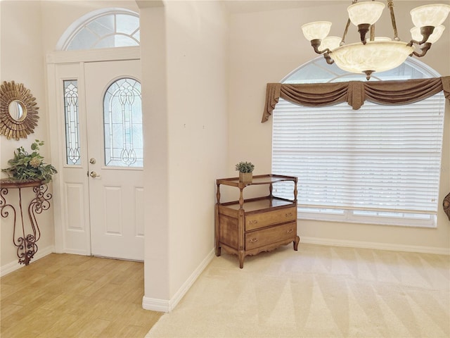 carpeted foyer featuring a healthy amount of sunlight, baseboards, a chandelier, and wood finished floors