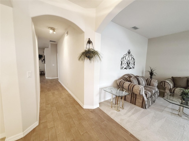 corridor featuring arched walkways, visible vents, light wood-style flooring, and baseboards