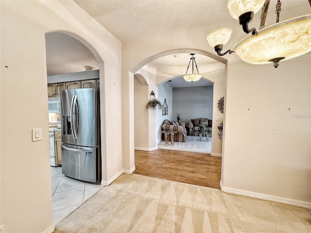 hallway with arched walkways, light colored carpet, a textured ceiling, and baseboards