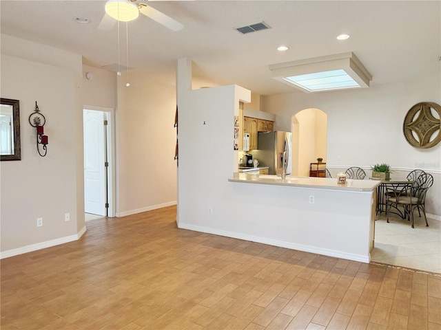 kitchen with arched walkways, light countertops, visible vents, light wood-style floors, and stainless steel fridge