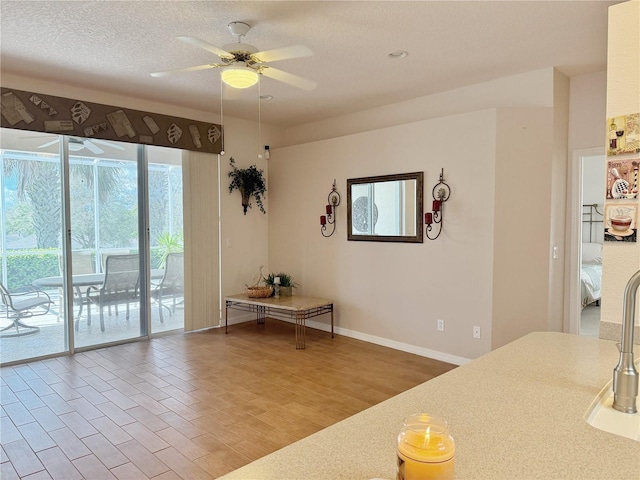 unfurnished dining area featuring ceiling fan, a textured ceiling, baseboards, and wood finished floors