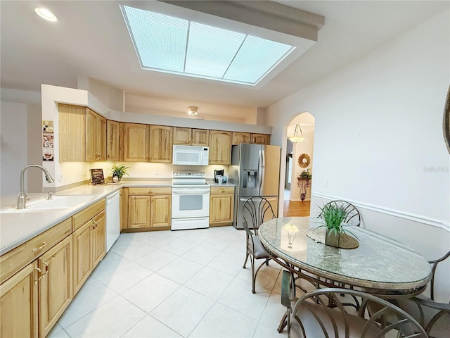 kitchen featuring a skylight, light tile patterned floors, light countertops, a sink, and white appliances