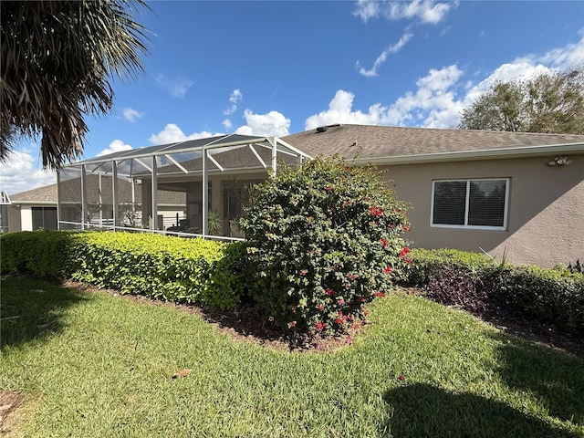 rear view of property featuring a lanai, a lawn, and stucco siding