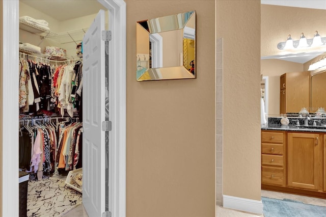 full bathroom with a textured wall, baseboards, a walk in closet, and vanity