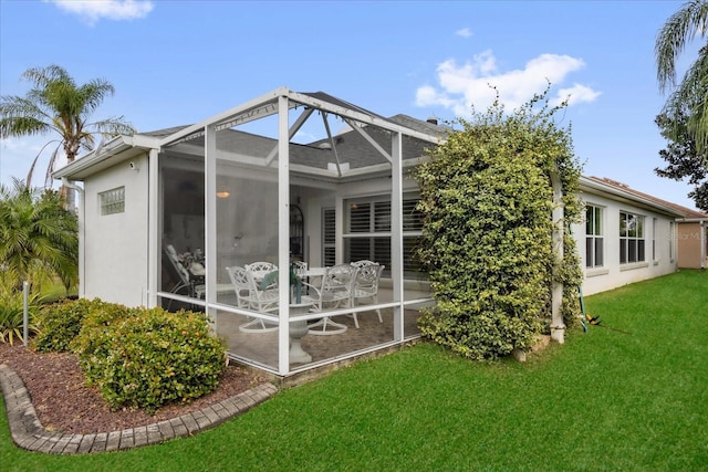 rear view of house featuring glass enclosure, a lawn, and a patio