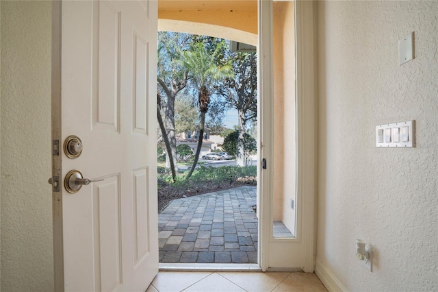 doorway to outside featuring light tile patterned floors and a textured wall