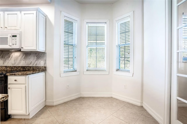 kitchen with light tile patterned floors, white microwave, baseboards, decorative backsplash, and dark stone countertops