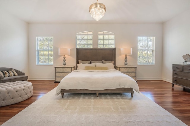 bedroom with a chandelier, multiple windows, baseboards, and wood finished floors