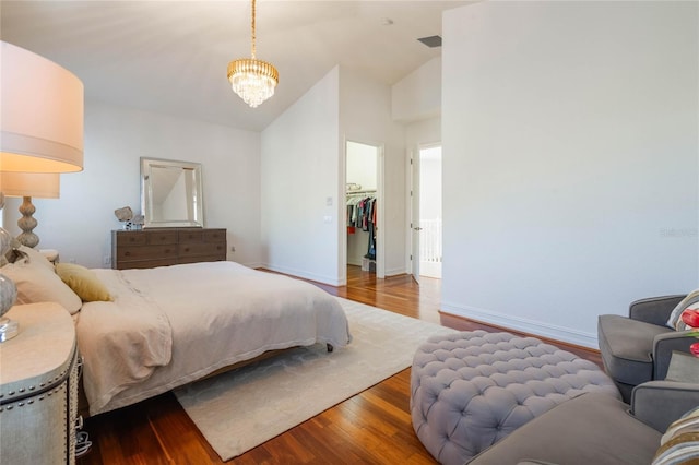 bedroom featuring a notable chandelier, a spacious closet, wood finished floors, high vaulted ceiling, and baseboards