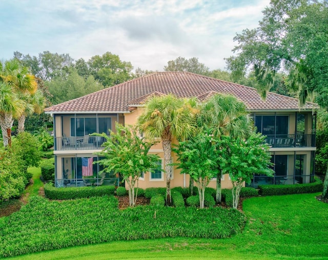 back of house featuring a lawn, a tile roof, a sunroom, and stucco siding