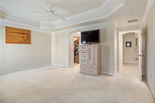 unfurnished bedroom featuring a tray ceiling, visible vents, arched walkways, and light colored carpet