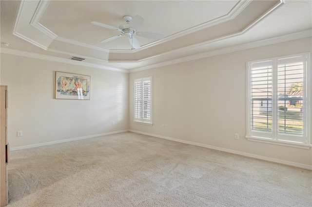 empty room featuring visible vents, a raised ceiling, a healthy amount of sunlight, and a ceiling fan